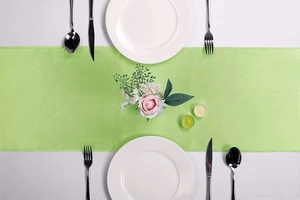 Flat lay of light green satin table runner with white ceramic plates for elegant dining decoration