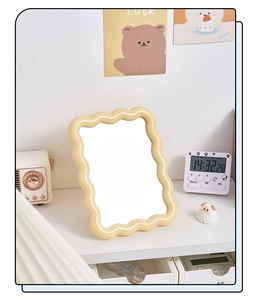 Detail view of a yellow wavy-edged makeup mirror on a desktop shelf in a cozy bedroom setting