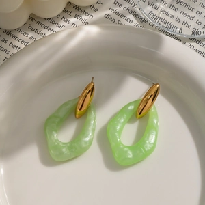 Close-up of gold metal and irregular green acrylic hoop earrings on a ceramic dish