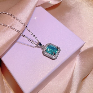 Elegant rectangle cut green gemstone necklace with diamond halo on pink satin background