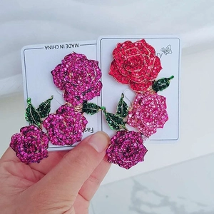 Detail of crystal rose flower earrings in pink and red with green enamel leaves