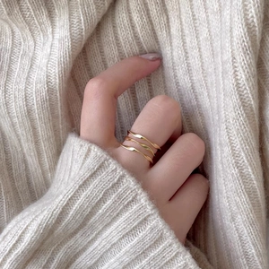 Close-up of three layered gold wavy rings worn on a hand with a cozy knit sweater