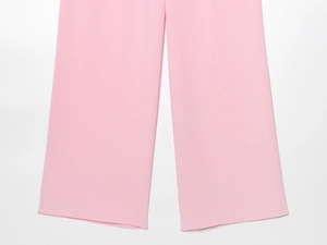 Détail d'un pantalon rose à jambes larges montrant le tissu lisse et les coutures de l'ourlet