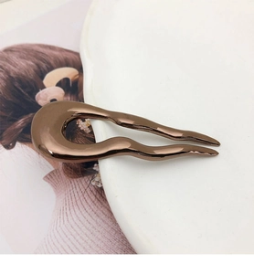 Close-up of minimalist brown metal U-shaped hairpin resting on a white plate edge