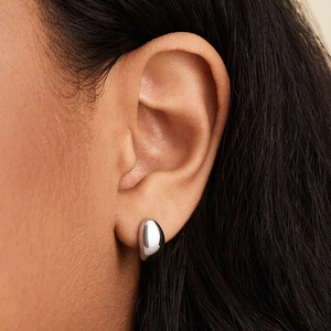 Macro view of water-drop silver stud earrings worn with a high-polished mirror finish