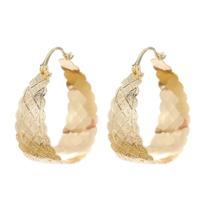 Close-up of golden hoop earrings featuring diamond patterns and scalloped wave edges