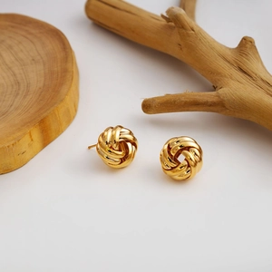 Detail view of gold woven knot earrings on natural wood and clean white background