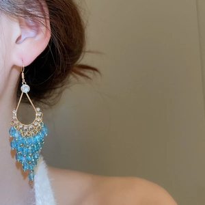 Close-up of golden teardrop earrings with light blue beaded fringe on model's ear
