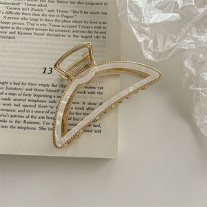 Detailed shot of golden metal mermaid hair claw clip on an open book with pearl texture