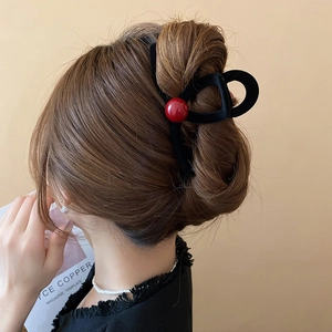 Detail of red bead on black flocked shark hair claw clip worn in a low bun hairstyle