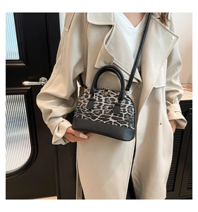 Detailed view of leopard print shell bag with black leather straps on a beige coat model