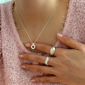 Detailed view of sterling silver necklace and rings set on a pink knit sweater