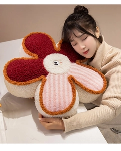 Large decorative plush flower cushion with smiley face held by a female model at home