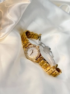 Detail of a luxury gold women's watch with rhinestone bezel on elegant white silk fabric
