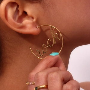 Close-up of a gold large hoop earring featuring 'rock' lettering on a female model