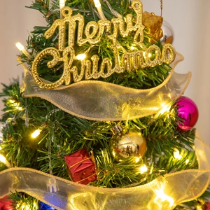 Close-up of golden Merry Christmas sign, LED lights and ornaments on a mini pine tree