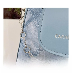 Close-up of light blue quilted crossbody bag with silver floral chain and denim texture