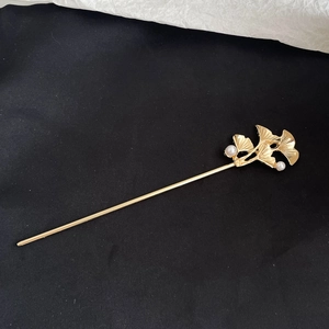 Detail of golden ginkgo leaf hair pin featuring textured metal leaves and white pearls