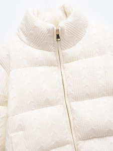 Detail of white knit jacket featuring heart patterns and premium golden zipper hardware