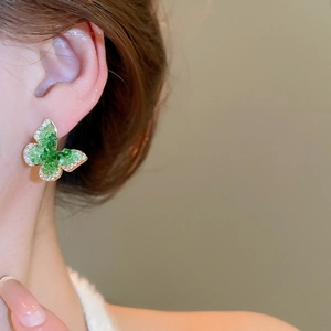 Detailed close-up of emerald green butterfly stud earring worn by model in golden finish