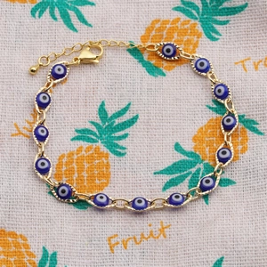 Detail view of a gold-plated evil eye bracelet with blue enamel charms on fabric background
