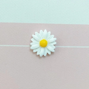 Macro shot of white daisy resin charm with yellow stamen on textured mint and pink fabric