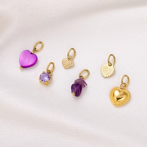 Detailed view of gold heart charms and purple stones on white silk fabric background