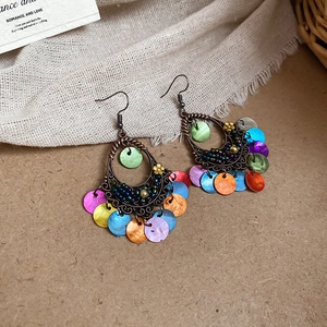 Detail of bohemian teardrop earrings with colorful shell tassels on rustic background