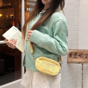 Close-up of yellow fabric crossbody bag featuring embroidered bows and metallic hooks