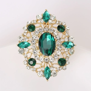 Macro shot of vintage gold brooch with emerald cut green stone and sparkling crystals