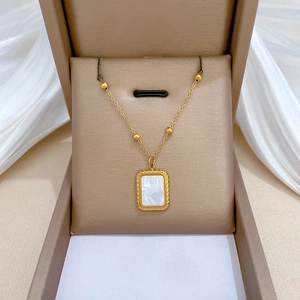 Detailed view of a gold square shell pendant necklace inside a beige jewelry gift box