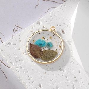 Macro detail of a round resin pendant featuring blue dried flowers and gold foil accents