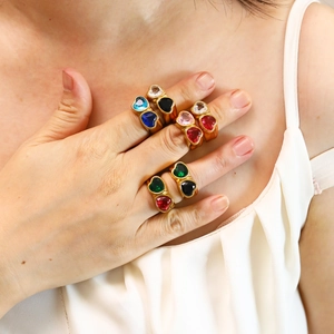 Close-up of golden double heart rings with colorful gemstones worn on hand