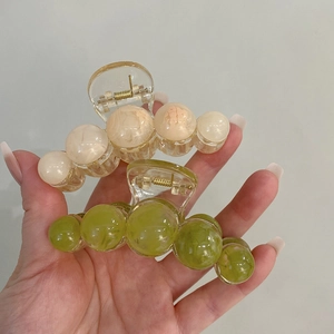 Detail shot of two gradient round bead shark clips held by hand against a white wall