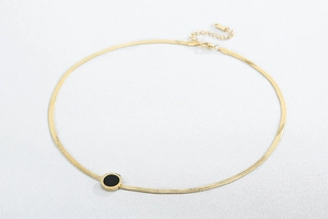Close-up of golden flat snake chain necklace with a black shell circular pendant