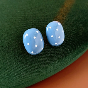 Dettaglio di orecchini ovali blu a pois bianchi su un supporto di velluto verde