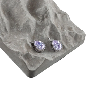 Pair of purple teardrop-shaped glass pendants with 18k gold plating on a stone background