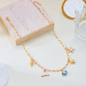 Gold paperclip chain necklace with sea shell, turtle, and starfish charms on a stone