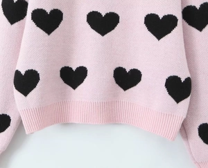 Detailed close-up of pink knit sweater featuring black heart patterns and ribbed hem finish