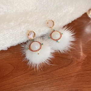 Detail of white plush ball earrings with pink gemstone and pearl embellishments