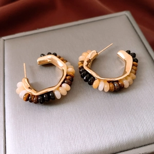 Detail view of 18K gold plated C-shaped earrings with tiger eye stone beads on velvet