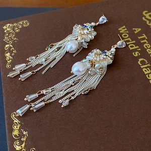 Detail of silver bow tassel earrings with baroque pearls and rhinestones on book