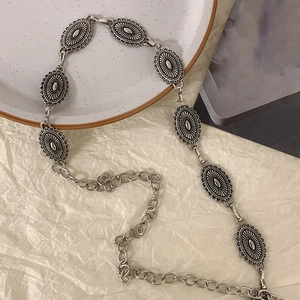 Gros plan d'une chaîne de taille vintage argentée avec breloques ovales sur plateau blanc