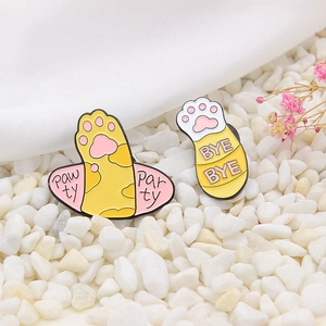 Cute set of two cat paw enamel pins featuring Pawty and Bye Bye slogans on white fabric