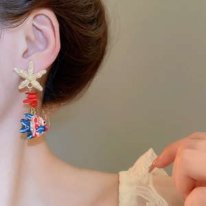 Detailed view of starfish and colorful fish earrings worn on a model for beach style