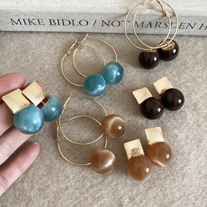 Detail view of resin hoop earrings and studs in amber and teal with golden metal