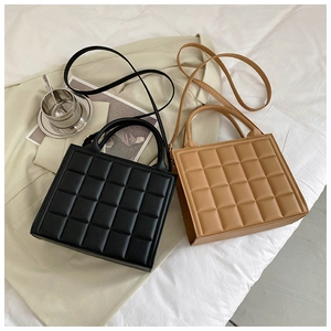 Flat lay of black and tan quilted leather square bags on beige blazer and white sheets