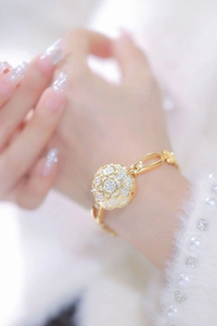 Close-up of a gold chain bracelet featuring a sparkling crystal camellia flower on a wrist