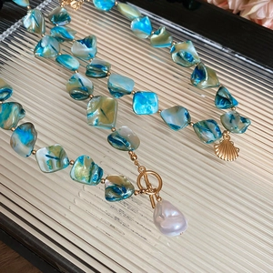 Macro view of blue shell beads with baroque pearl pendant and golden toggle clasp
