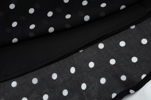 Detailed macro view of black polka dot chiffon fabric with double-layer stitching finish